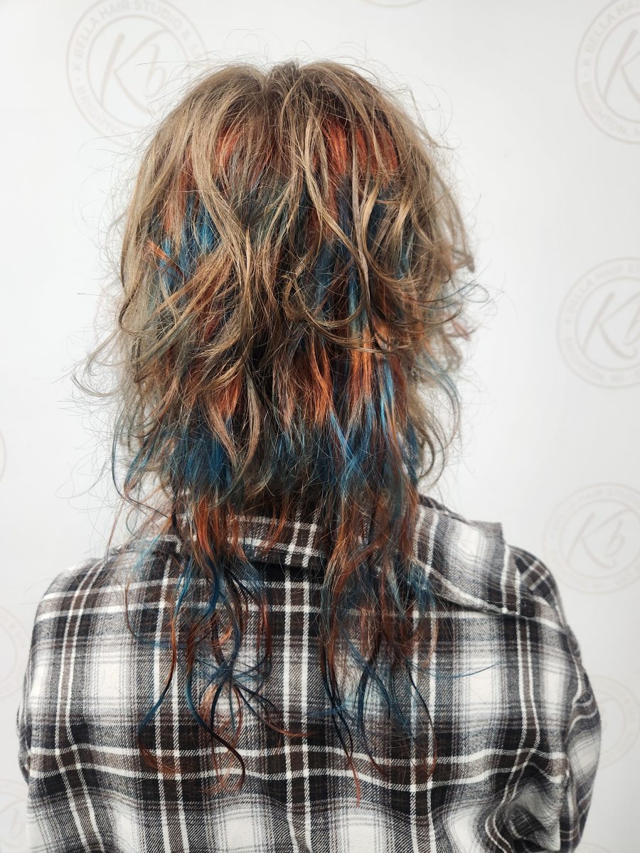 Back view of shoulder-length hair with shaggy layers, vivid red-orange and blue color, and braided rattails, by Siobhan Rozinski at K Bella Hair Studio & Spa in Brighton, MI