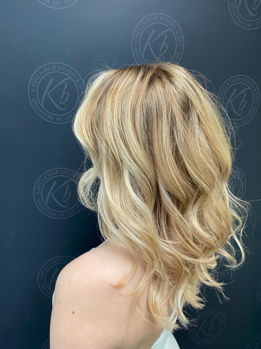 Back view of blonde balayage with darker rooting and lighter dimension throughout the wavy lengths, by Abbey French at K Bella Hair Studio & Spa in Brighton, MI