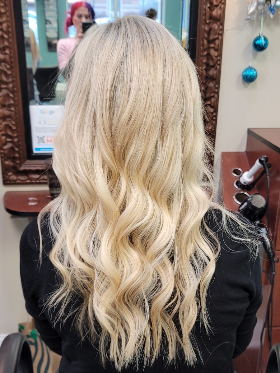 Rear view of long blonde wavy hair with extensions, styled in loose waves, by Kristan Sayers at K Bella Hair Studio & Spa in Brighton, MI