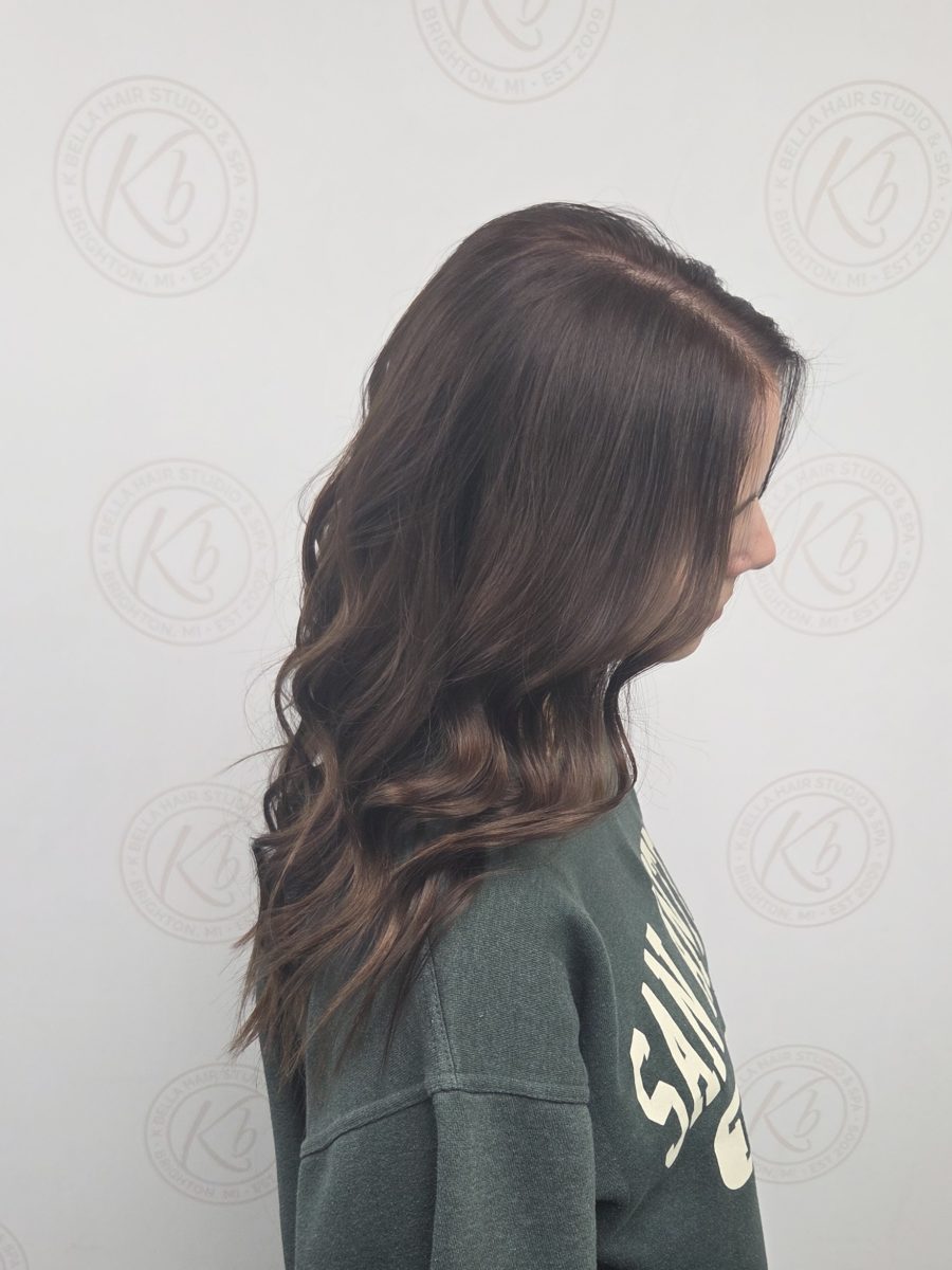 Side view of long wavy hair with dimension and chestnut tones by Katie Rowe at K Bella Hair Studio & Spa in Brighton, MI