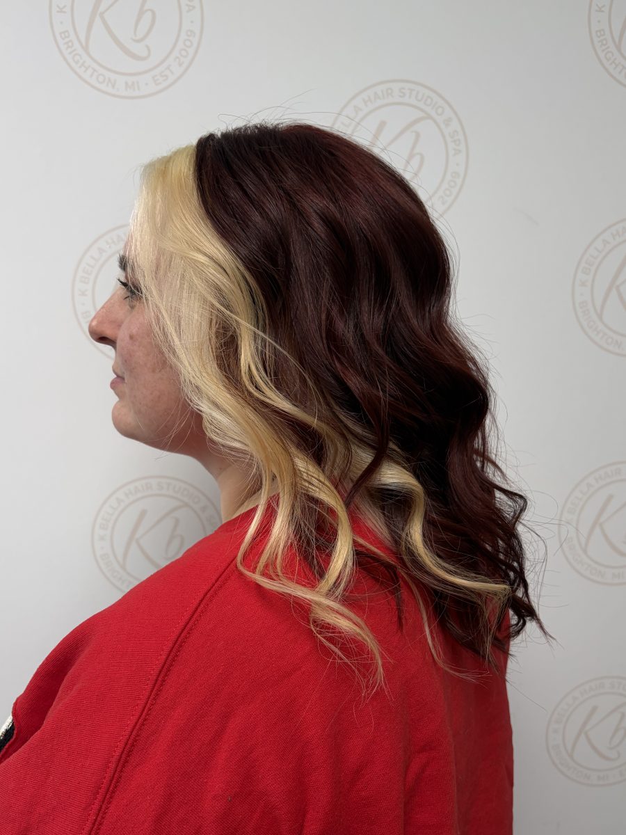 Three-quarter back view of wavy hair showing blonde highlights woven through burgundy base by Abbey French at K Bella Hair Studio & Spa in Brighton, MI