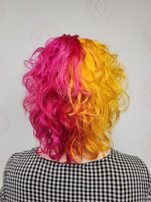 Back view of shoulder-length hair with hot pink and golden yellow color blocking and layered texture by Siobhan Rozinski at K Bella Hair Studio & Spa in Brighton, MI