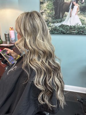 Side view of long wavy hair with dimensional blonde and gray tones after keratin extension installation by Liberty Greenwood at K Bella Hair Studio & Spa in Brighton, MI