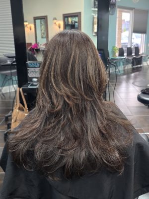 Back view of long layered hair with chocolate brown base color and caramel balayage highlights by Kristan Sayers at K Bella Hair Studio & Spa in Brighton, MI