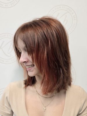 Profile view of chin-length shag bob with layered texture and side-swept bangs, warm mahogany tones, by Kristan Sayers at K Bella Hair Studio & Spa in Brighton, MI