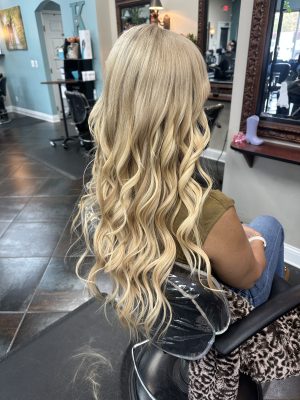 Back view of long blonde hair with soft waves, showing volume weft extensions by Kameryn Bell at K Bella Hair Studio & Spa in Brighton, MI