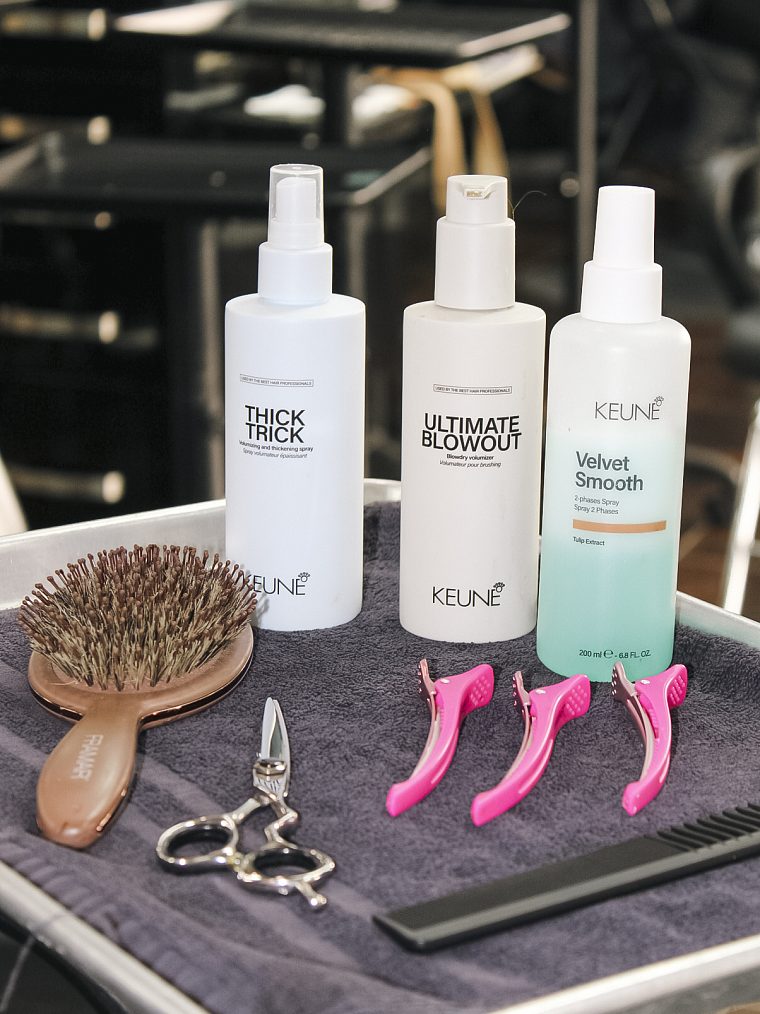 A stylist tray laid out with a brush, shears, sectioning clips and Keune styling sprays